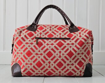 May include: A red and beige patterned travel bag with brown leather accents. The bag has a zipper closure and brown leather handles. The corners of the bag are reinforced with brown leather.