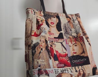 May include: A tote bag featuring a collage of magazine-style portraits and text including words like Beauty, Lifestyle, and Creativity. The bag has a rectangular shape with dark brown shoulder straps and a woven fabric texture with a multi-colored print.