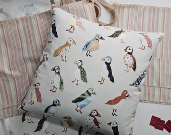 May include: A white throw pillow with a colorful pattern of puffins. The puffins are depicted in various poses and colors, including blue, green, red, and yellow. The pillow is made of a soft, comfortable fabric and would be a great addition to any home.
