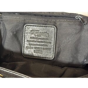 May include: Black leather handbag interior with a zipper and a rectangular leather tag. The tag features the Fossil logo and text: "All Fossil products are handcrafted from the finest top grain leathers available. Genuine leather product 76082."