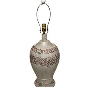 May include: A beige ceramic table lamp with a decorative geometric pattern in red, green, and black. The lamp has a white finial and a metal lamp harp. The base is round and the lamp is approximately 18 inches tall.