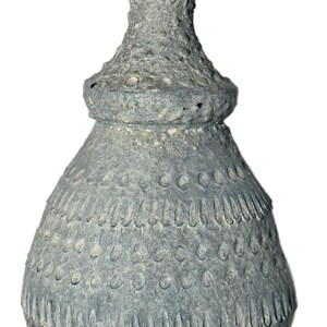 May include: A textured, gray ceramic lamp base with a bulbous shape and a detailed, layered design. The lamp base has a rough, pitted surface and a silver-colored metal fitting at the top. The overall aesthetic is rustic and artisanal.