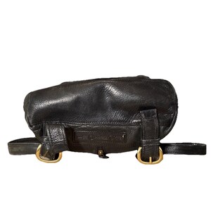 May include: Black leather backpack with gold-colored buckles and hardware. The bag has a rounded shape and adjustable straps. The leather appears to be slightly distressed, giving it a vintage look. The bag has a small zipper closure.