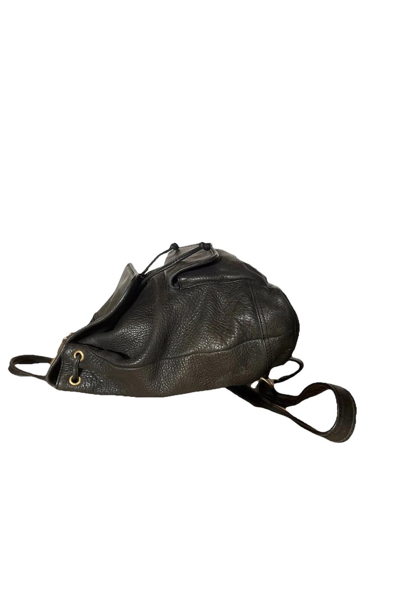 May include: Black leather drawstring backpack with a textured surface. The bag features gold-colored eyelets and adjustable shoulder straps. The bag is designed with a top flap and a drawstring closure.