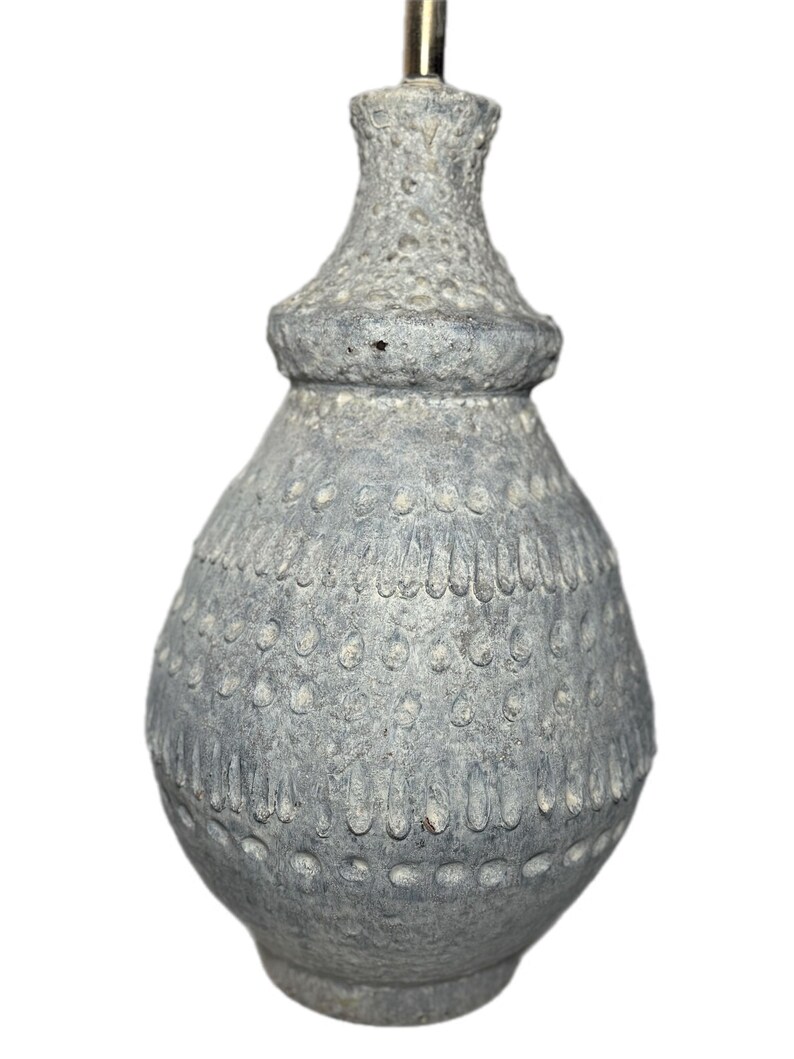 May include: A gray ceramic lamp base with a textured surface and a decorative pattern of small circles and vertical lines. The lamp base has a bulbous shape with a narrower neck and a metal rod at the top.