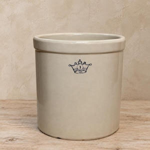 May include: A cylindrical off-white stoneware crock featuring a smooth, glazed finish and a thick, reinforced rim. A dark blue graphic of a crown with the number 1 inside and the text USA underneath is centered on the front of the vessel.