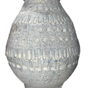 May include: A gray decorative vase with a textured surface and a bulbous body. The vase features a series of vertical and circular patterns around the body. The vase has a wide base and a narrow neck.