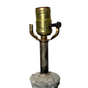 May include: A vintage lamp base with a textured, gray stone-like appearance. The lamp features a brass-colored socket and a black switch. The lamp is designed to hold a light bulb and provide illumination.