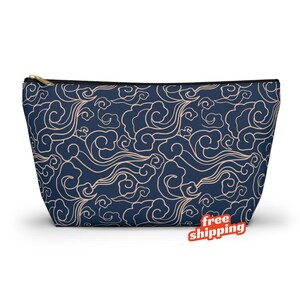 May include: A navy blue zippered pouch with a beige cloud pattern. The pouch has a black zipper and a gold-colored zipper pull. The cloud design is a repeating pattern across the entire surface of the pouch.