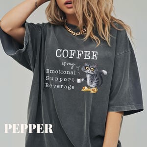 May include: Dark grey t-shirt featuring the text "COFFEE is my Emotional Support Beverage" and a cartoon cat with a coffee cup. The word "PEPPER" is printed at the bottom of the shirt.