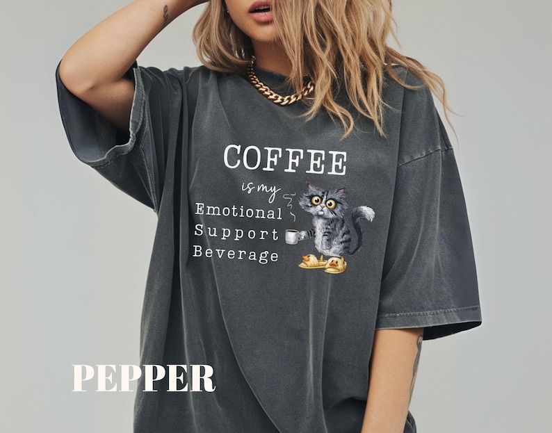 May include: Dark grey t-shirt featuring the text "COFFEE is my Emotional Support Beverage" and a cartoon cat with a coffee cup. The word "PEPPER" is printed at the bottom of the shirt.
