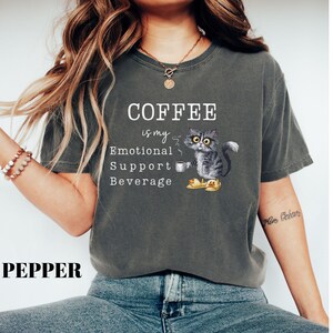 May include: Dark grey t-shirt featuring the text "COFFEE is my Emotional Support Beverage" and a cartoon cat with a coffee cup. The word "PEPPER" is printed at the bottom of the shirt.