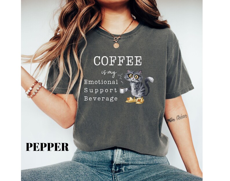 May include: Dark grey t-shirt featuring the text "COFFEE is my Emotional Support Beverage" and a cartoon cat with a coffee cup. The word "PEPPER" is printed at the bottom of the shirt.