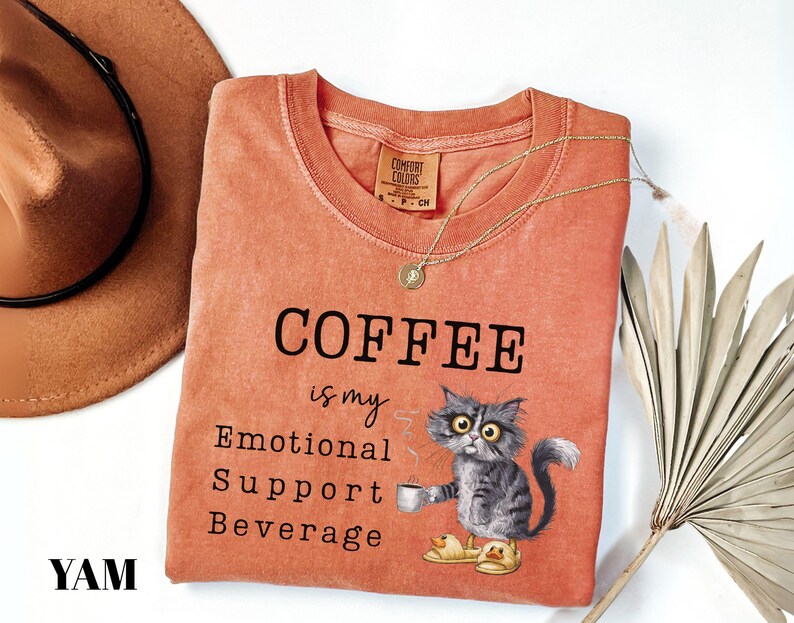 May include: Orange Comfort Colors t-shirt with the text "COFFEE is my Emotional Support Beverage." A cartoon cat wearing slippers and holding a coffee cup is printed on the shirt. A gold necklace is draped across the shirt.