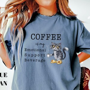 May include: Blue jean coloured t-shirt with the text "COFFEE is my Emotional Support Beverage". The shirt features a cartoon cat holding a coffee cup and wearing slippers. The cat is grey and white.