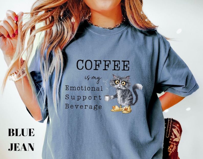 May include: Blue jean coloured t-shirt with the text "COFFEE is my Emotional Support Beverage". The shirt features a cartoon cat holding a coffee cup and wearing slippers. The cat is grey and white.