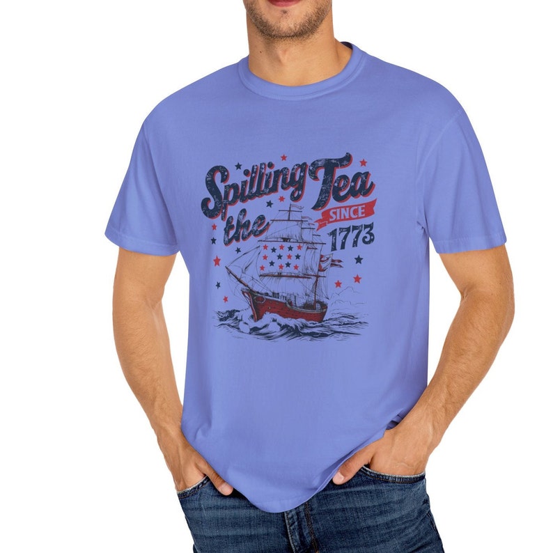 May include: A light blue t-shirt with a vintage-style graphic of a ship sailing on the water. The graphic includes the text "Spilling Tea the Since 1773".