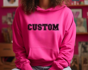 May include: A bright pink hoodie with a black "CUSTOM" graphic printed on the front. The hoodie has a drawstring hood and a kangaroo pocket.
