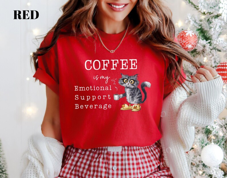 May include: Red t-shirt featuring the text "COFFEE is my Emotional Support Beverage" and a cartoon cat illustration. The cat is grey and white with yellow eyes, holding a coffee cup. The shirt has short sleeves.
