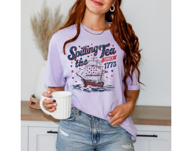 May include: A lavender t-shirt with a vintage-style graphic of a ship with the text "Spilling the Tea Since 1773".