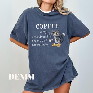 May include: Denim blue t-shirt with the text "COFFEE is my Emotional Support Beverage." The shirt features a graphic of a cat holding a coffee cup. The cat is wearing yellow slippers. The word "DENIM" is printed at the bottom.