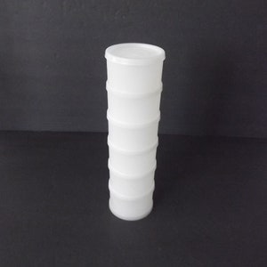 May include: A tall, white plastic container with a lid. The container is cylindrical, composed of stacked sections, and sits upright against a dark background. The design suggests a storage or organizational product.