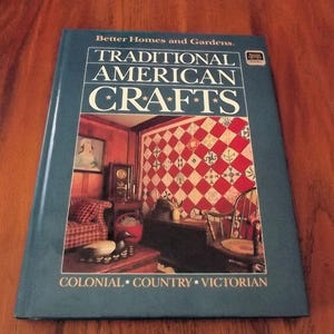 May include: A teal book titled "Traditional American Crafts" by Better Homes and Gardens. The cover features a detailed interior scene with a red and white quilt, a sofa, and a chair. The book's subtitle reads "Colonial, Country, Victorian."