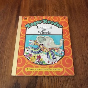 May include: A vintage Little Golden Book titled "Eager Reader Elephant on Wheels." The cover features a cartoon elephant wearing a colorful outfit and roller skates. The book has an orange background with a floral design and the text "A book you can read by yourself."