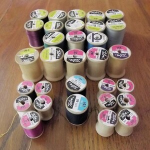 May include: A collection of vintage Talon sewing thread spools in various colors including purple, blue, grey, and white. Each spool features a circular paper label on top with the Talon brand name, color numbers, and prices printed in black text.