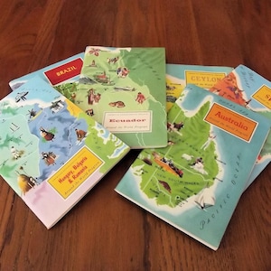 May include: A collection of six vintage Around the World Program booklets featuring illustrated maps of countries including Hungary, Bulgaria, Rumania, Ecuador, Brazil, Ceylon, Australia, and Spain, each with a rectangular title label on the cover.