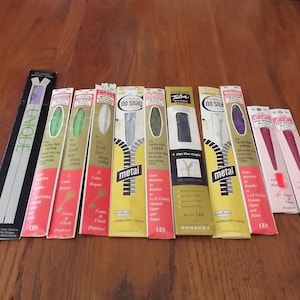 May include: A collection of vintage metal zippers in various colors, including green, white, and purple, displayed in their original packaging. The packaging features text such as "No Snag" and "Talon" and the brand names "Coats & Clark".
