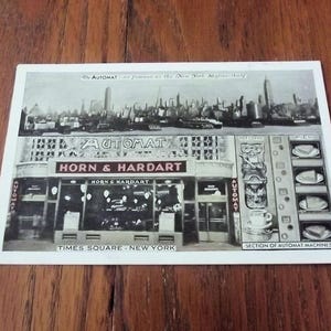 May include: Black and white vintage postcard featuring the Horn & Hardart Automat in Times Square, New York. The image shows the restaurant's facade, the Automat machines, and the New York skyline.