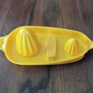 May include: A bright yellow citrus juicer set. The set includes a tray with a built-in reamer, a small reamer, and a textured area for removing seeds. The juicer is made of plastic and is designed for easy use.