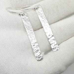May include: A pair of silver hammered bar earrings with hoop closures.