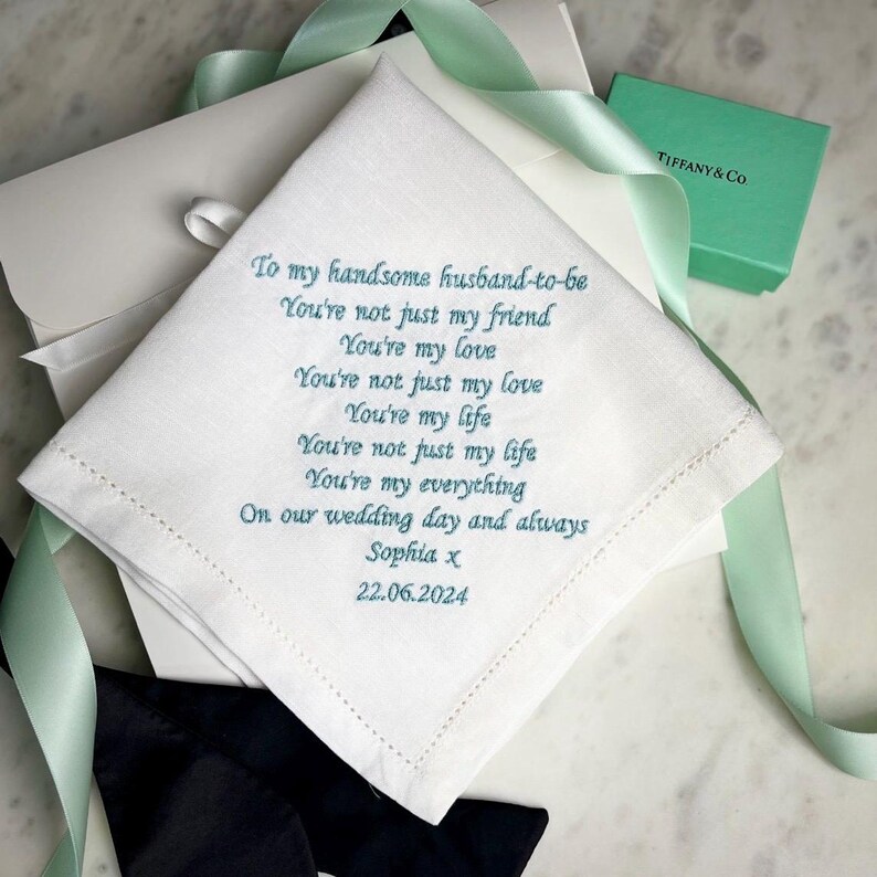 May include: A white square handkerchief featuring teal embroidered text that reads: To my handsome husband-to-be, You're not just my friend, You're my love, You're not just my love, You're my life, You're not just my life, You're my everything, On our wedding day and always, Sophia x, 22.06.2024.