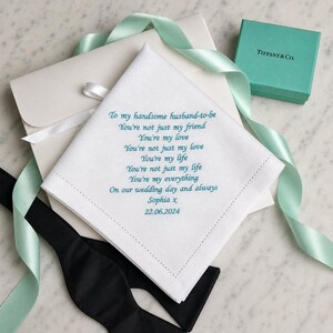 May include: A white square handkerchief with teal embroidered text that reads: To my handsome husband-to-be, You're not just my friend, You're my love, You're not just my love, You're my life, You're not just my life, You're my everything, On our wedding day and always, Sophia x, 22.06.2024.
