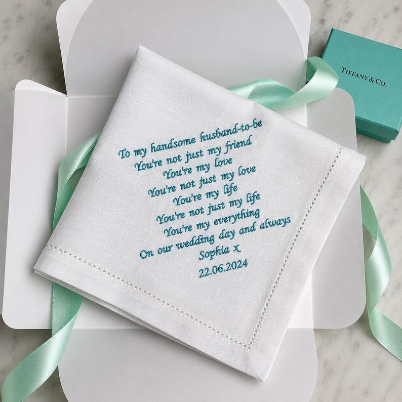 May include: A white square handkerchief with teal embroidered text that reads: To my handsome husband-to-be, You're not just my friend, You're my love, You're not just my love, You're my life, You're not just my life, You're my everything, On our wedding day and always, Sophia x, 22.06.2024.