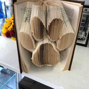Könnte beinhalten: Ein Buch mit Seiten, die zu einer Pfotenabdruckform gefaltet sind. Das Buch ist geöffnet und die Seiten sind gefaltet, um einen dreidimensionalen Pfotenabdruck zu erstellen.