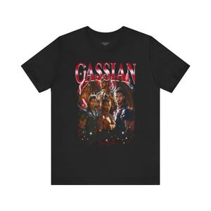 May include: Black t-shirt featuring a graphic of several men with wings and the name "CASSIAN" in red and white lettering. The design has a fantasy theme with a red and white lightning bolt effect.