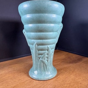May include: A teal green ceramic vase with a ribbed design and a leafy pattern at the base.