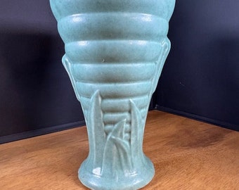 May include: A teal green ceramic vase with a ribbed design and a leafy pattern at the base.
