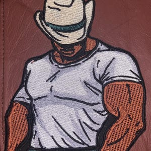 Può includere: Toppa ricamata di una persona che indossa un cappello da cowboy bianco, una maglietta bianca e jeans blu. La persona ha la pelle marrone ed è di spalle.