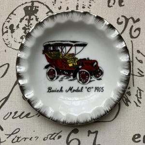 Puede incluir: Platillo pequeño, blanco, con borde festoneado y borde dorado. El centro presenta una ilustración de coche antiguo en rojo, amarillo y negro, con el texto "Buick Model 'C' 1905". Una pieza decorativa para coleccionistas.