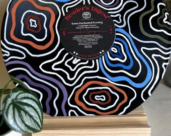 May include: A black vinyl record with a white stand. The record is painted with a swirling pattern of blue, orange, purple, and white lines on a black background. The record label says "Reader's Digest" and "Some Enchanted Evening - Candlelight Classics - Music for Quiet Listening".