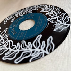 May include: A black vinyl record with a white fern design painted on it. The label is blue and says "RCA VICTOR" and "I Don't Believe In Tomorrow".