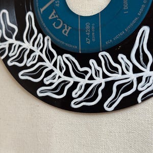 May include: A black vinyl record with a white fern design painted around the edge. The label is blue and has the text "RCA" and "47-4280 (ELVW-3291)" printed on it.