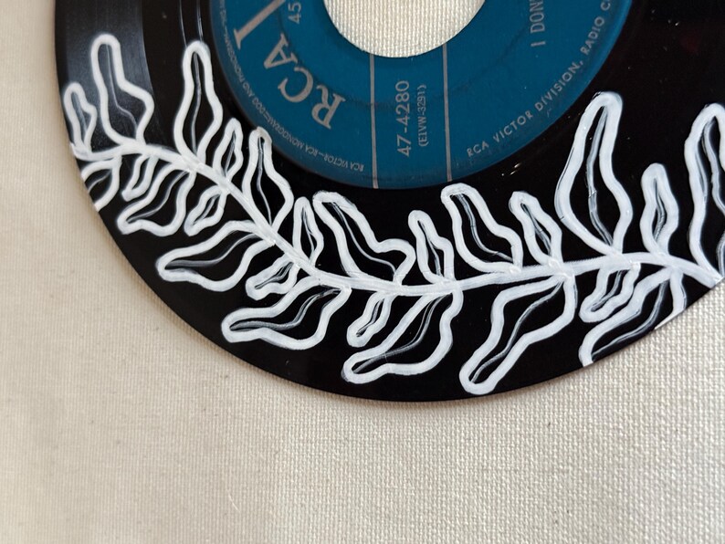 May include: A black vinyl record with a white fern design painted around the edge. The label is blue and has the text "RCA" and "47-4280 (ELVW-3291)" printed on it.