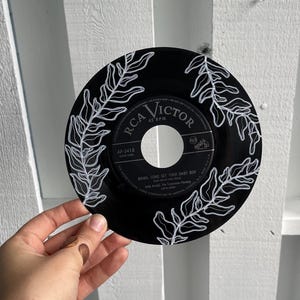 May include: A black vinyl record with white painted fern leaves. The record label is for RCA Victor and the song is "Mama, Come Get Your Baby Boy" by Little Anthony and The Imperials.