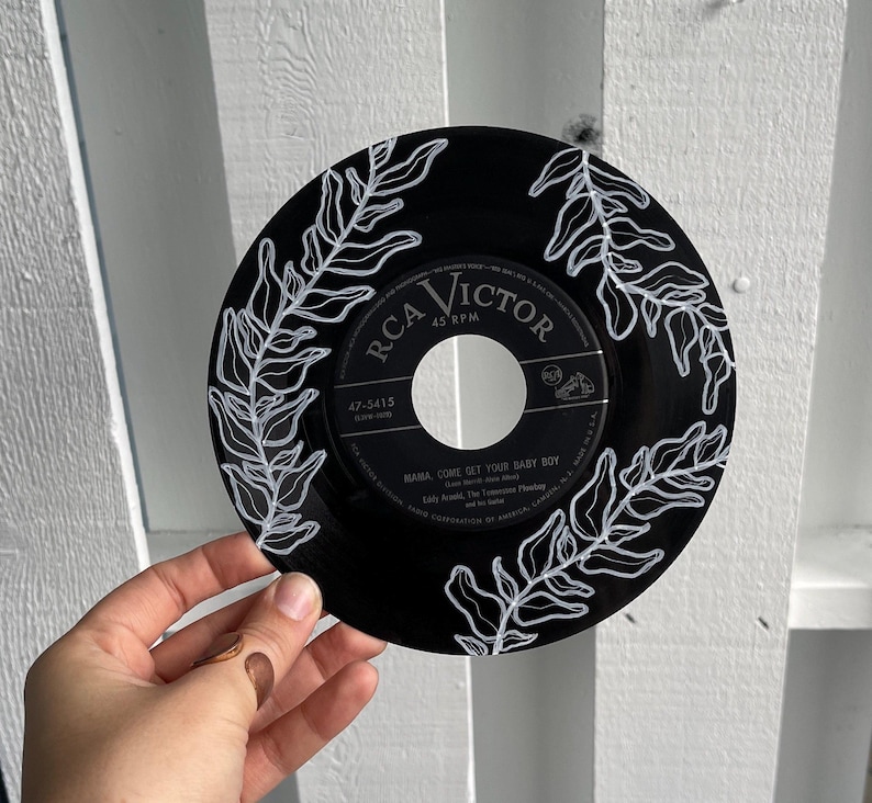 May include: A black vinyl record with white painted fern leaves. The record label is for RCA Victor and the song is "Mama, Come Get Your Baby Boy" by Little Anthony and The Imperials.