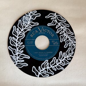May include: A black vinyl record with white painted fern designs. The record label is blue and says "RCA Victor 45 RPM" and "47-4280". The song title is "I Don't Believe In Tomorrow" by Savannah Churchill.